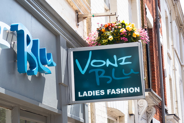 a sign on a shop saying Voni Blu Ladies Fashion sticking out at right angles, with another sign perpendicular saying Blu