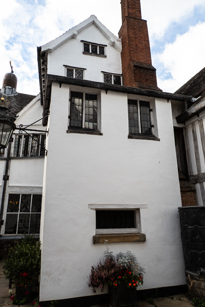 a white building with two windows at the top, and one at the bottom with a brick chimney and another white building just showing behind.